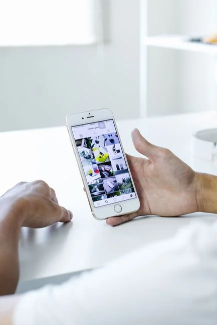 about-us-02 Hand holding smartphone displaying digital wallet app interface, blurred monitor in background.